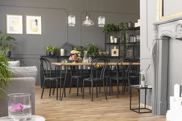 Lamps above table and black chairs in grey dining room interior with posters and plants. Real photo