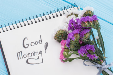 Good morning wish concept. Bouquet of statice limonium flowers and notepad with good morning wish. Blue background.