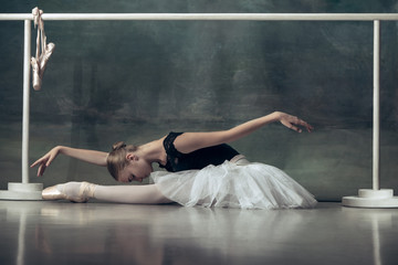 The classic ballet dancer in white tutu posing at ballet barre on studio background. Young teen...