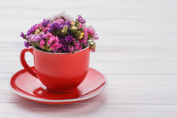 Limonium statice flowers bouquet in coffee mug. White wood background.