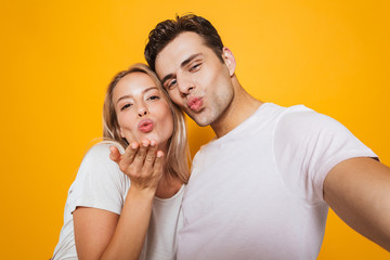Naklejka premium Loving couple standing isolated over yellow wall background take a selfie by camera.