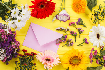 Collection of different flowers and post mail. Yellow wooden desk background.