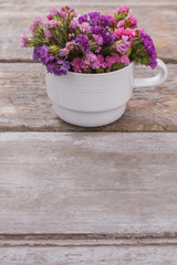 Fototapeta na wymiar Colorful statice flowers in white coffee cup. Old vintage wooden desk surface background.