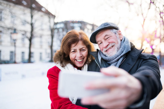 Senior couple with smartphone on a walk in a city in winter.