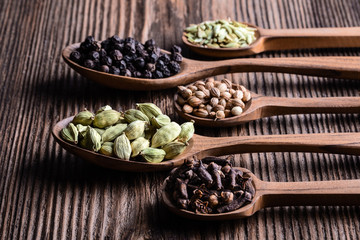 Different types of whole Indian spices in wooden spoons on rustic background close-up.