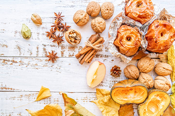 backed apples in foil with walnuts, autumn leaves and cinnamon on white wooden background