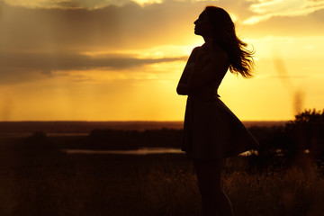 silhouette of girl at sunset in summer field, a young woman enjoying nature