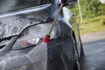 Mann sprüht Autoshampoo bei Autowäsche in Auto SB Waschbox mit Hochdruckstrahler auf