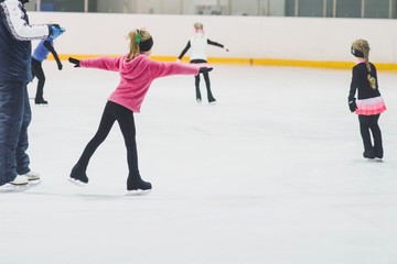 Little girls learning to ice skate. Figure skating school. Young figure skaters practicing at indoor skating rink. - obrazy, fototapety, plakaty