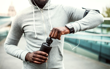 A close-up of young sporty black man runner with water bottle in a city.
