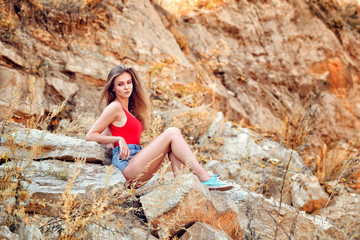 Beautiful young woman sitting on the rock, in the afternoon, in hot weather