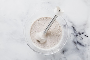 prepare batter for pancakes in a glass bowl with a hand blender on a marble table