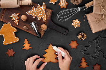 Woman decorating gingerbread Christmas cookies with icing sugar. Christmas preparations concept. Top view with copy space.
