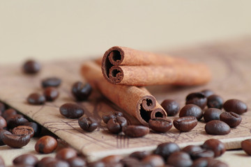 Two cinnamon sticks lie on a beige stand, which is located on the table, on a light background. Coffee beans lie around 