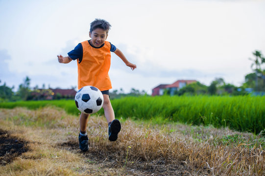 8 Or 9 Years Old Happy And Excited Kid Playing Football Outdoors In Garden Wearing Training Vest Running And Kicking Soccer Ball