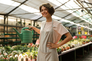 Woman gardener standing over plants in greenhouse water flowers