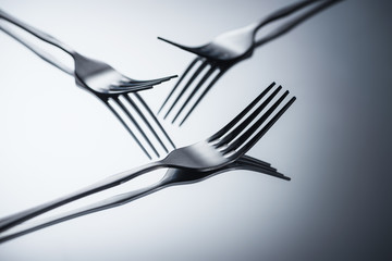 close-up view of three shiny forks reflected on grey