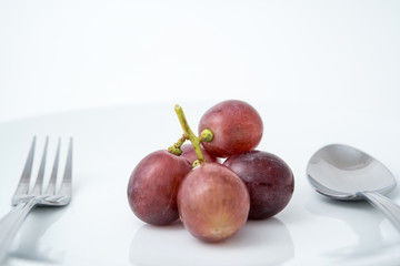 health eating of fruit, red grape on white plate with fork and spoon