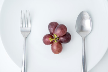 health eating of fruit, red grape on white plate with fork and spoon
