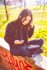 young beautiful woman outdoor listening music with headphones and smart phone using tablet -...