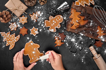 Woman decorating gingerbread Christmas cookies with icing sugar. Christmas preparations concept. Top view with copy space.