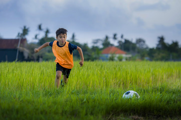 Fototapeta premium 8 or 9 years old happy and excited kid playing football outdoors in garden wearing training vest running and kicking soccer ball