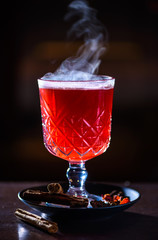 Hot cranberry drink with lemon, cinnamon and other spices on dark background