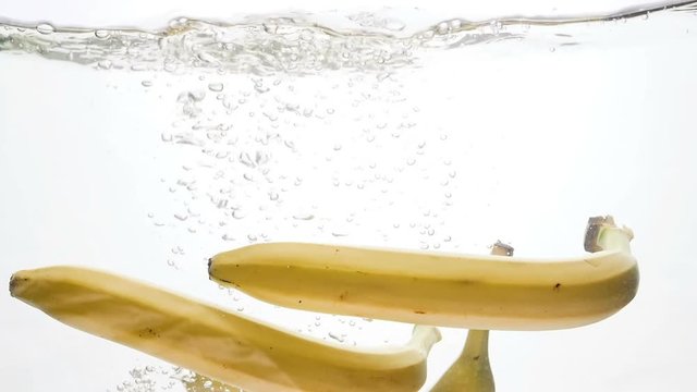 Slow motion footage of fresh ripe bananas falling under water against white background. Air bubbles floating up