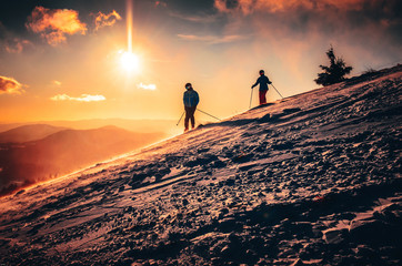 Couple silhouette in ski resort. Warm sunset in background. Skiing in two