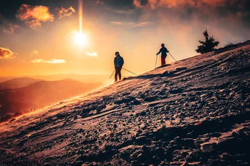 Fotobehang Couple silhouette in ski resort. Warm sunset in background. Skiing in two © kovop58