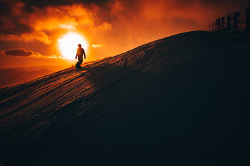 Snowboarder in ski resort. Winter sport photo. Orange sunset light in background. Edit space. Christmas and New Year time, snowy photo, edit space