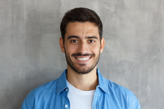 Indoor photo of handsome European guy pictured isolated on grey background standing close to camera with dark face hair and short haircut, looking satisfied and happy, spending his leisure time