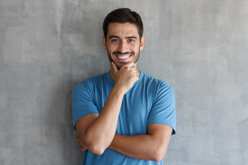 Obraz premium Indoor photo of young handsome European Caucasian man isolated on gray background standing with arms crossed and looking attentively at viewer, smiling confidently, willing to listen with interest