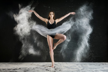 Fototapeta na wymiar beautiful slender girl with long hair dancing in a dark Studio in a cloud of dust