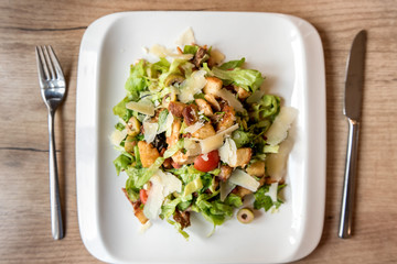 Plate of Caesar salad with utensils on restaurant wooden table