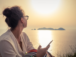 Fototapeta premium Young woman using smartphone at sunset in front of the sea on Ponza island coast
