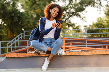 Woman sitting outdoors in park using mobile phone listening music with earphones.