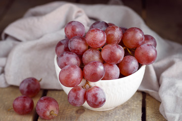 Bowl with pink grapes on a wooden stand.