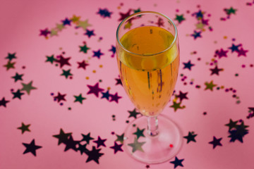 glass of champagne on a pink background with star confetti