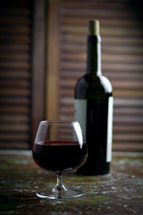 wine glass with expensive red wine,  blurred bottle of wine, wooden background
