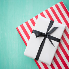 Fototapeta premium Closeup of beautiful Christmas gifts wrapped in white and striped gift paper decorated with ribbon on turquoise wooden table. New Year, holidays and celebration concept