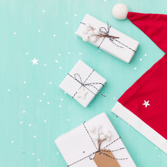 Closeup of nice Christmas gifts wrapped in white paper, Christmas tree decorations,  Santa's hat on wooden background with sparkling stars. New Year, holidays and celebration concept
