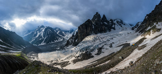 Summer mountain panorama in Western Caucasus. Ahsu glacier, snow covered mountains near Ushba and rocks against stormy sky.