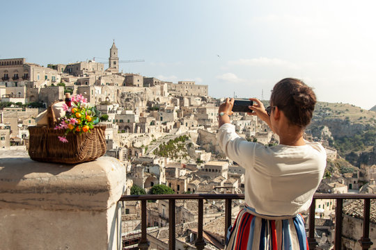 Young elegant woman tourist in historical Matera town in Italy taking photos with smartphone
