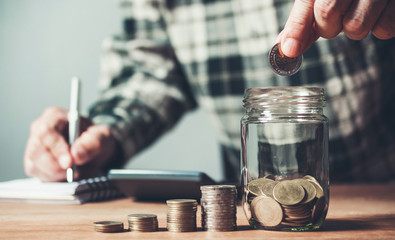Business man putting coin in glass bottle saving bank and account for his money all in finance accounting concept.