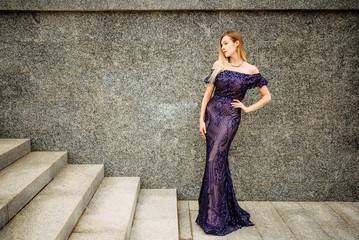 Fashionable portrait of style. Young beautiful woman in a blue long dress posing on the stairs...