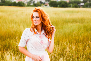 Fototapeta na wymiar Portrait of a young red-haired woman in a tall yellow grass at sunset.