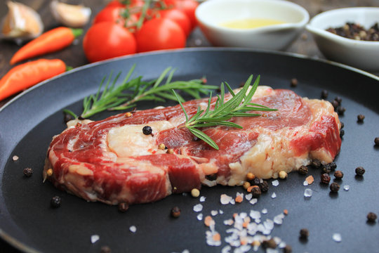 Raw beef steak with rosemary in frying pan and vegetables on wooden dark background, food meat or barbecue