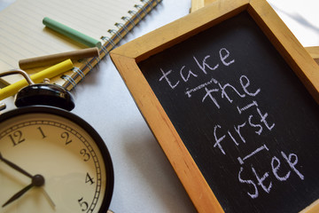 Take the first step phrase colorful handwritten on chalkboard, alarm clock with motivation and education concepts.