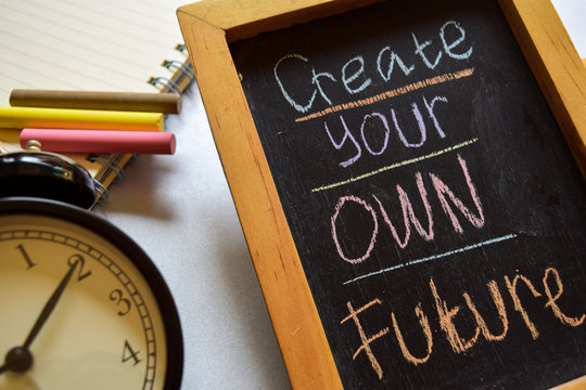 Create your own future on phrase colorful handwritten on chalkboard, alarm clock with motivation and education concepts.